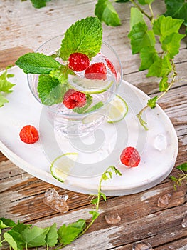 Summer alcohol fresh drink. Raspberry mint cocktail, slice of lime, ice cubes and raspberry on a natural wooden surface, Outdoor.