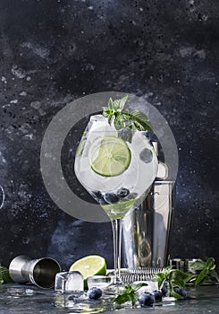 Summer alcoholic cocktail blueberry mojito with rum, green mint, lime and crushed ice, bar tools, gray bar counter, selective