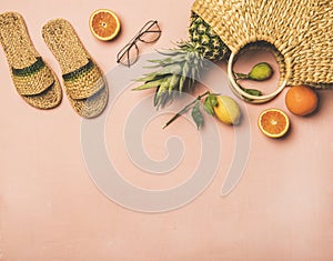 Summer apparel items and fresh fruits over pastel pink background