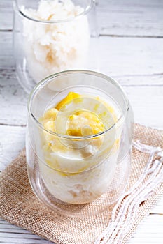 Summer appetizer of Thailand concept. Durian and sticky rice with coconut milk cream in transparent glass on white wooden table