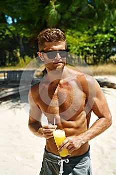 Summer. Athletic Muscular Man Drinking Juice Cocktail On Beach