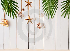 Summer background with beach sand, starfish coconut leaves, and shell decoration hanging on wooden background