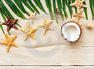 Summer background with beach sand, starfish coconut leaves, and shell decoration hanging on wooden background