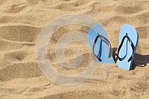 Summer background of beach and shoes on sand. Blue flip flops on the sunny tropical beach.