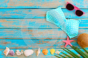 Summer background with bikini, sunglasses, coconut, starfish, coral and shells on blue wooden background.