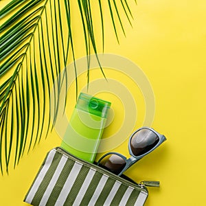 Summer background. Composition striped beach cosmetic bag with sunblock and sunglasses on a yellow background. Summer