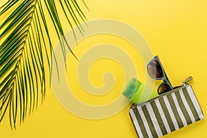 Summer background. Composition striped beach cosmetic bag with sunblock and sunglasses on a yellow background. Summer