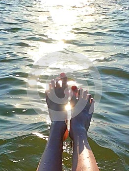 Summer background. Female legs in sea against background of reflection of sunlight in water