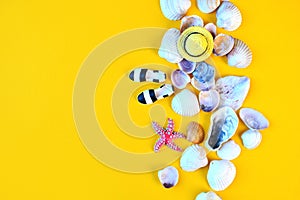 Summer background. Flat lay traveler beach accesories on yellow background with seashells, miniature hat and moccasins.