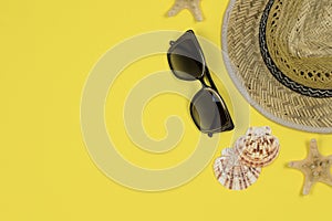 Summer background. Straw sun hat, sunglasses and seashells on a yellow background.