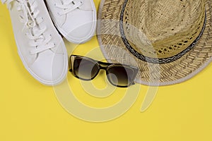 Summer background. Straw sun hat, sunglasses and white sneakers on a yellow background.