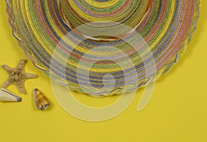 Summer background. Striped hat all colors of the rainbow and seashells on a yellow background.
