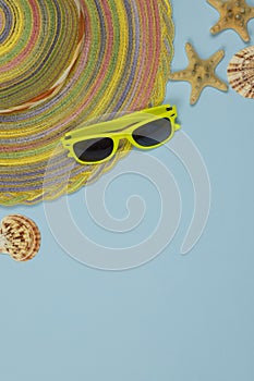 Summer background. Striped hat, yellow glasses and seashells on a light blue background.