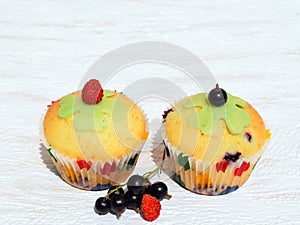 Summer baking - delicious homemade muffins with berries in colorful paper cups, decorated with marzipan cloverleaf and fruits