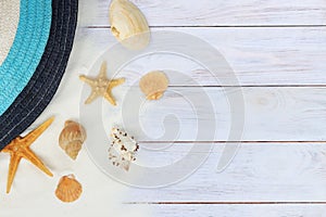 Summer banner with a hat, seashells and starfish on a wooden light background with sand