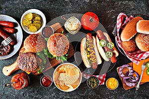 Summer BBQ food table with hot dog and hamburger buffet, flat lay over a dark background