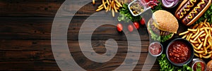 Summer BBQ food table scene with a dark wood background showing a top view of hot dogs and hamburgers buffet