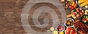 Summer BBQ or picnic food corner border over a rustic wood banner background, overhead view with copy space