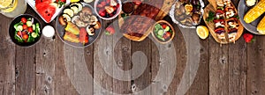 Summer BBQ or picnic food top border over a rustic wood banner background, above view with copy space