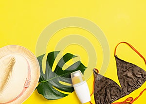 Summer beach accessories sunscreen summer hat swimsuit bright yellow background. Summer holiday concept and beach.