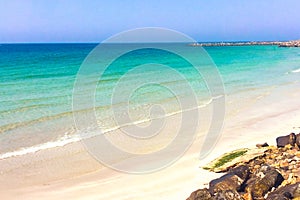 Summer beach background.  Rocky beach with black stones. White beach and green sea background. Nature background