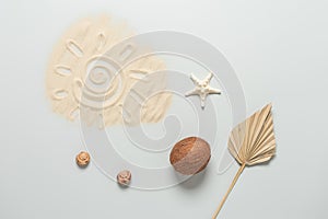 Summer beach composition. Drawing of the sun on the sand, coconut, starfish, seashells and dry palm leaf on a gray background. Top