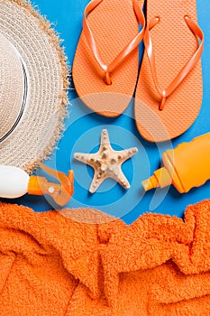 Summer beach flat lay accessories. Sunscreen bottle cream, straw hat, flip flops, towel and seashells on colored Background.