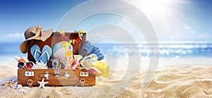 Summer Beach Preparation - Suitcase And Accessories With Sand And Defocused Glittering On Sea