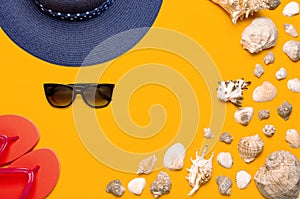 Summer beach sea accessories. Coral flip flops, blue straw hat, sunglasses, shells, starfish on yellow background top view flat