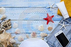 Summer beach sea concept. Blue Wooden background with different accessories, shells, starfish, towel, sunscreen, sand