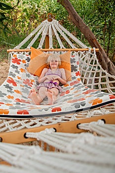 Summer beach tropical vacation with kids. Cute happy little caucausian girl laying in a hammock