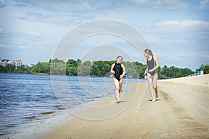 In the summer afternoon on the beach, two girls girlfriends play on the banks of the river