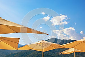 Summer beach vacation, concept. Sun beach umbrellas against mountains and blue sky with light white clouds