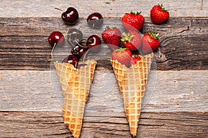 Summer berries in ice cream cones on wooden background.