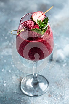 Summer berries smoothie strawberries and raspberry in glass with mint leaf and raw beeries on blue background. vertical image. top photo