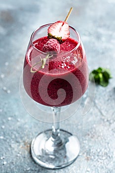 Summer berries smoothie strawberries and raspberry in glass with mint leaf and raw beeries on blue background. vertical image. top photo