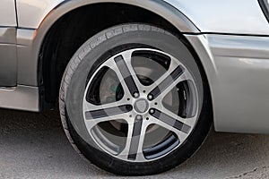 Summer black tire under the wing of a black car close-up with an alloy aluminium disk. Seasonal wheel replacement in a car