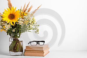 Summer bouquet of wildflowers in glass vase, old books on rustic background. Season design concept. Teachers day concept, back to