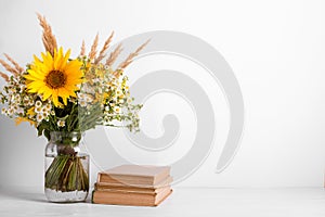 Summer bouquet of wildflowers in glass vase, old books on rustic background. Season design concept. Teachers day concept, back to