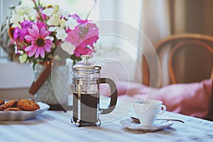 Summer breakfast in cozy country house. Table with bouquet of flowers from own garden, french press with coffee and cookies.