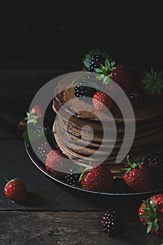 Summer breakfast with pancakes, strawberries, blackberries on old wooden table, vertical