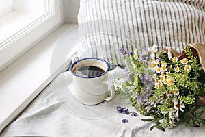 Summer breakfast scene. Enamel mug, wild flowers bouquet and linen cushion. Vintage feminine photo, rustic design