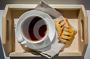 Summer breakfast. White cup with tea, butter biscuits on a wooden tray on a white table. View from above