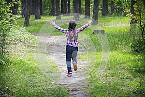 In the summer, on  bright sunny day in the forest, a small happy girl runs along the path