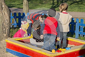 In summer, a bright and sunny day a lot of small children playing in the sandbox.