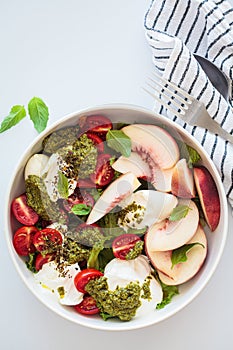 Summer burrata salad with peaches, cherry tomatoes, pesto and spices in bowl on white background