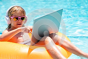 Summer business. Child working on laptop in summer pool. Little freelancer using computer, remote working in poolside.