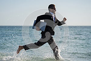 Summer business. Freelancer run on summer sea beach. Businessman in wet suit jump in sea water. Crazy business summer