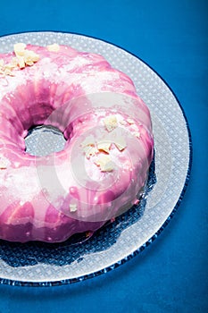 Summer cake with sugar pink glaze on a glass plate. Blue background