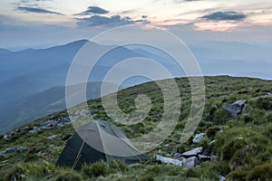 Summer camping in mountains at dawn. Tourist tent on round grass